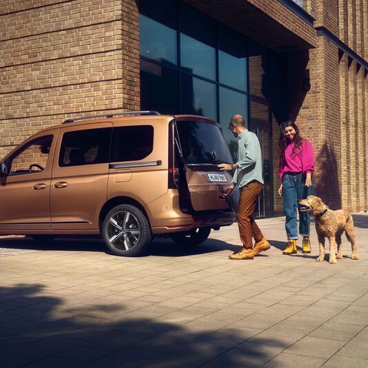 Ein weißer Caddy Kastenwagen fährt dynamisch durch eine belebte Stadt.
