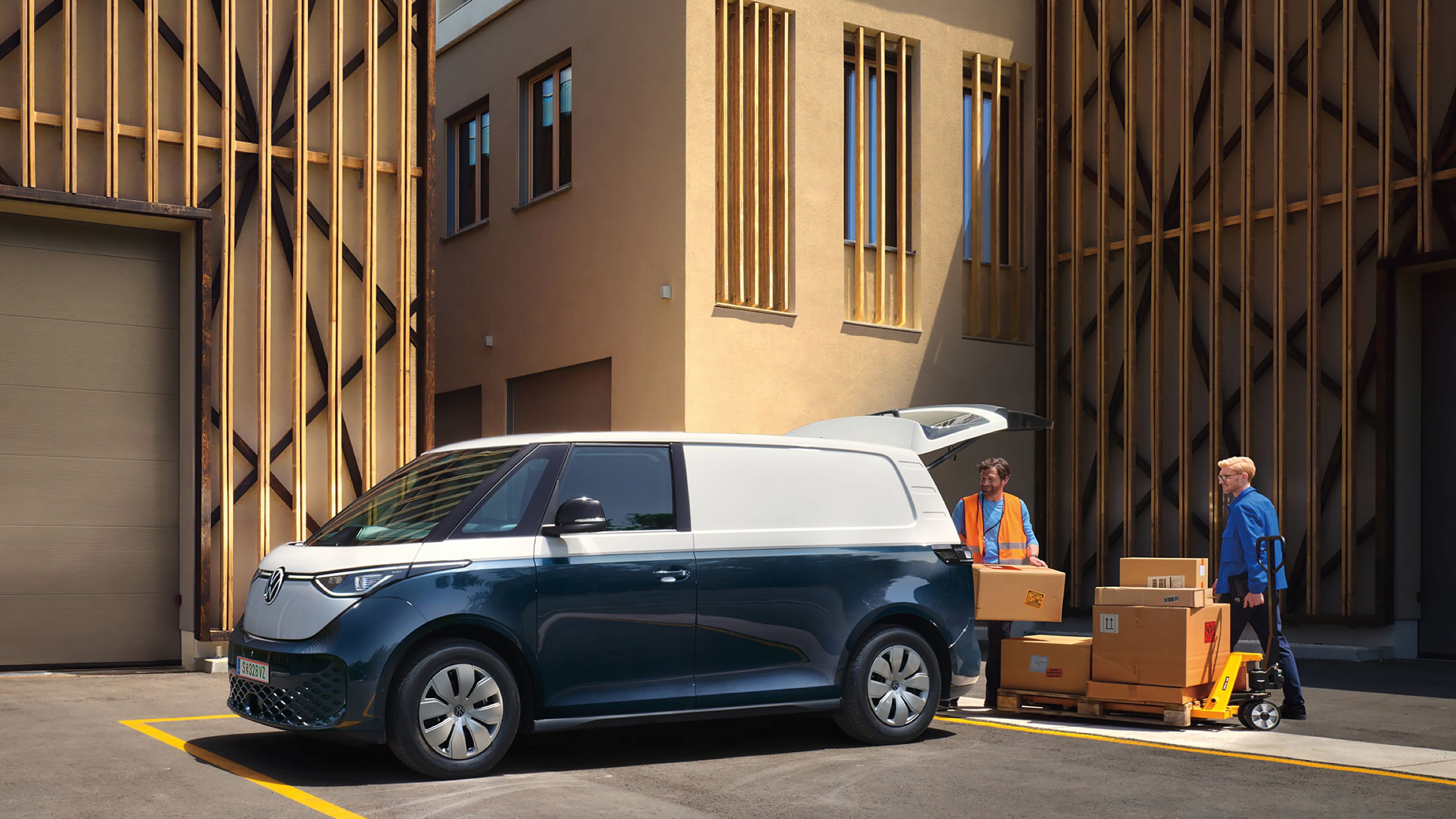 Zwei Personen beladen einen weiß blauen ID. Buzz Cargomit Kartons durch das Heck