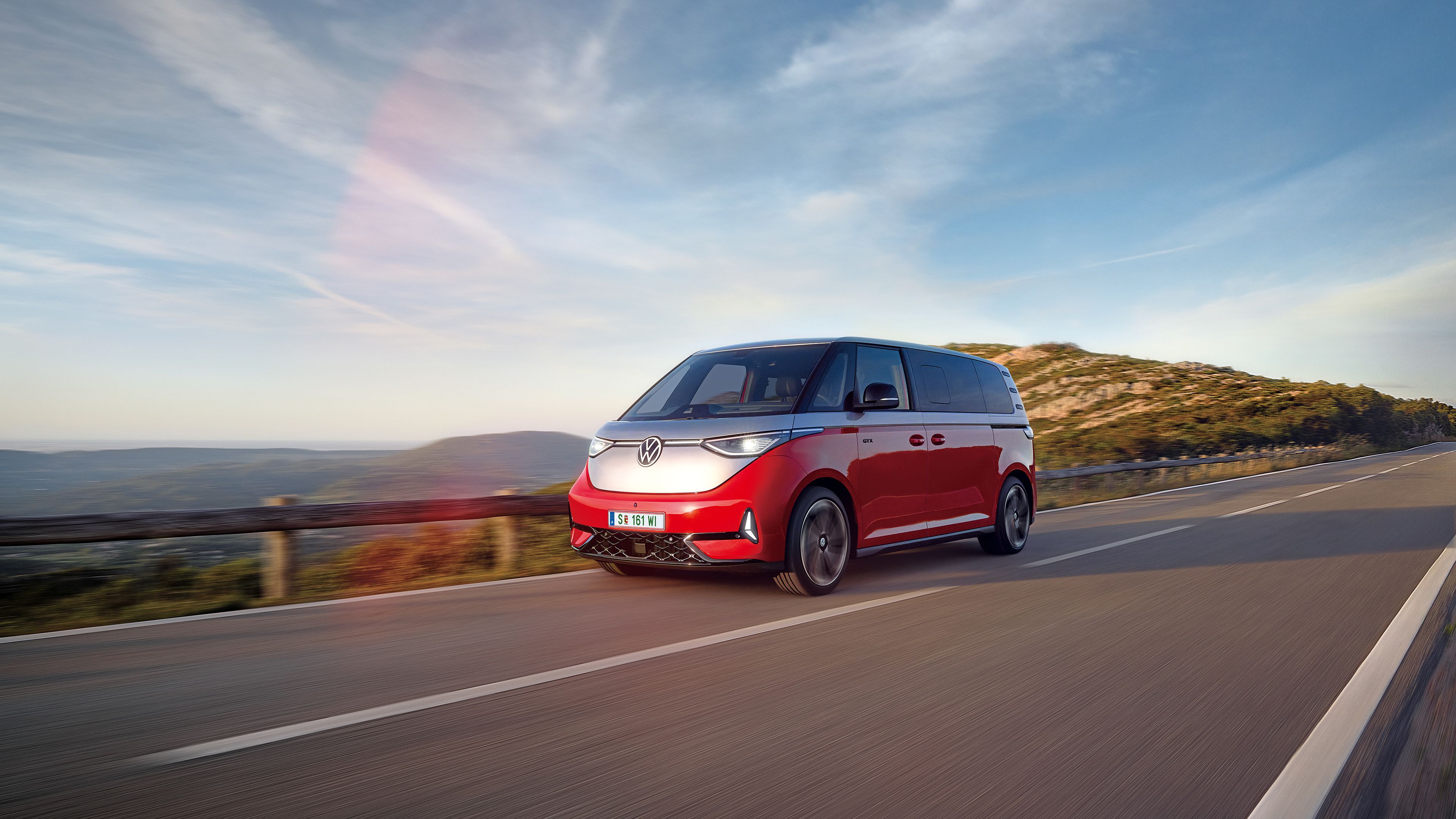 Ein rot - silberner ID. Buzz fährt entlang einer Straße in den Bergen