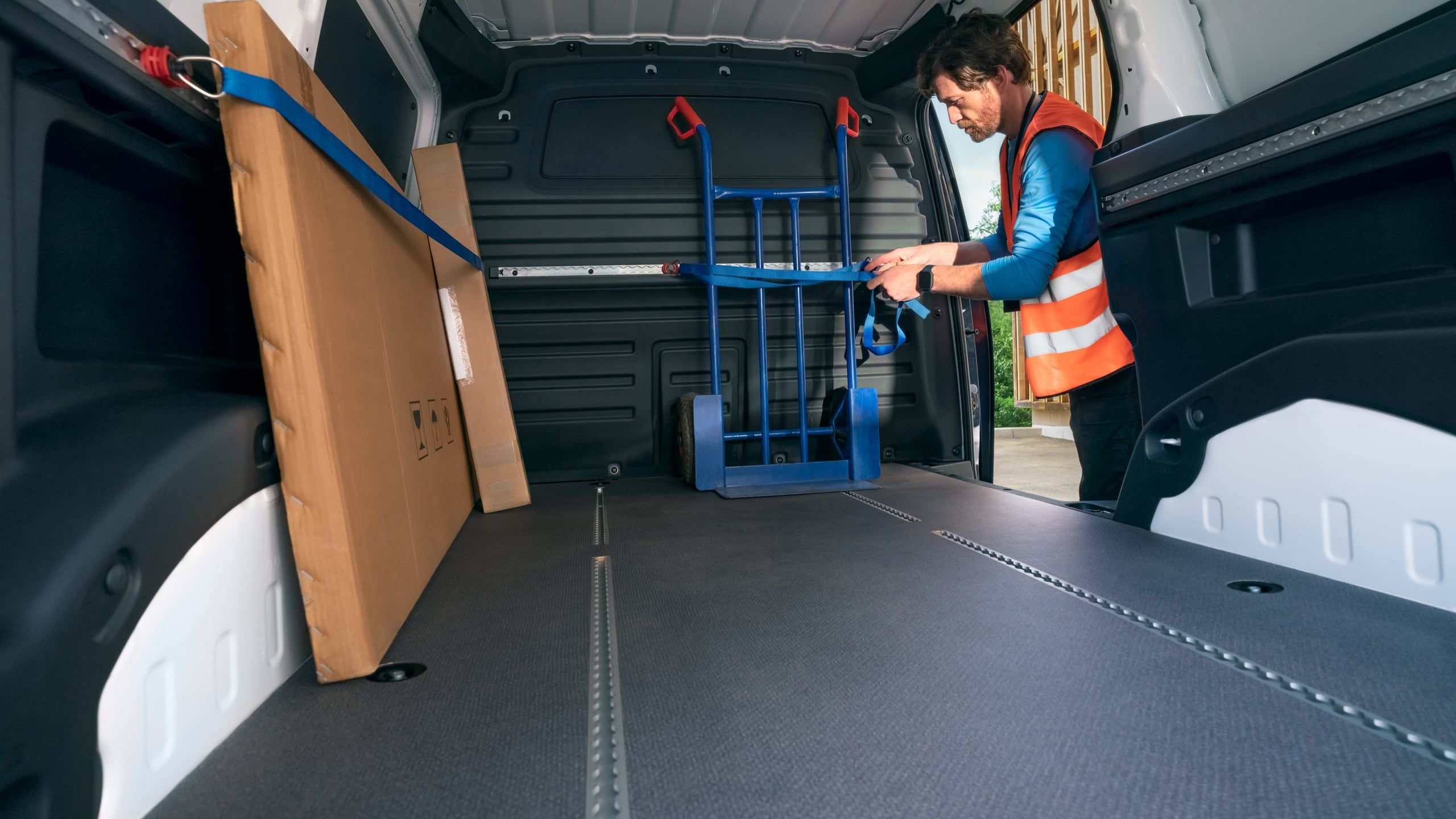 Eine Sackkarre wird im Laderaum eines ID. Buzz Cargo mit Hilfe des Schienensystems verzurrt