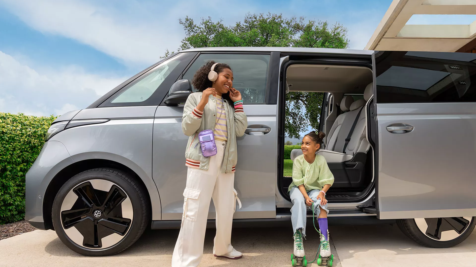 ID. Buzz mit geöffneten Schiebetüren parkt vor einem Haus, Kinder davor